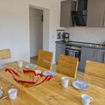 Essbereich mit Holztisch und Stühlen. Küche mit grauen Schränken und Edelstahlgeräten.