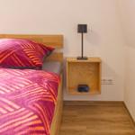 Schlafzimmer mit Bett, Nachttisch und Lampe. Holzfußboden und Wandbeleuchtung.