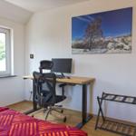 Zimmer mit Schreibtisch, Bett und Wandbild. Fenster mit Blick auf Grün.