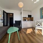 Wohnbereich mit Sofa, Esstisch und Küchenzeile. Holzboden und Wandbild sichtbar.