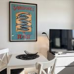 Tisch mit zwei Stühlen, Fernseher und Wandbild mit Sardinenmotiv.