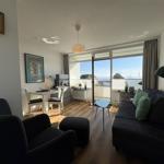 Wohnzimmer mit Sofa, Sessel und Blick auf Balkon mit Meerblick.
