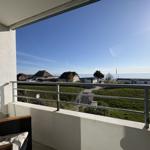 Balkon mit Sicht auf Strand und Meer unter blauem Himmel.