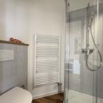 Bad mit Dusche, Toilette und Heizkörper an der Wand.
