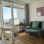 Wohnzimmer mit Sofa, Tisch und Blick aufs Meer durch Balkontür.