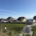 Grüner Hang mit Steigweg zum Strand. Im Hintergrund Häuser und Meer.