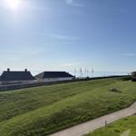 Grüner Hang mit Weg, Blick auf Strandhaus und Meer unter blauem Himmel.