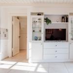 Wohnbereich mit weißem Schrank, Fernseher und Holzofen. Tür führt in einen anderen Raum.