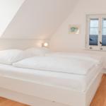 Ein Schlafzimmer mit Doppelbett, zwei Fenstern und Holzboden.