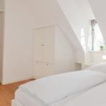 Schlafzimmer mit weißem Bett, Kleiderschrank und Dachschrägenfenster.