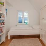 Schlafzimmer mit weißem Bett, Bücherregal und Kleiderschrank unter schrägem Dach