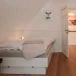 Schlafzimmer mit Bett, Wandbild und Holzboden. Tür führt in einen Flur.
