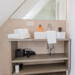Badezimmer mit Waschbecken, Spiegel und Handtuchstapel unter Dachschräge.