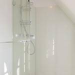 Dusche mit Glaswand, Duschbrause und Handbrause. Weiße Wände und Boden.