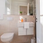 Badezimmer mit Waschbecken, Spiegel, Toilette und Dusche.