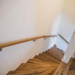 Holztreppe mit Handlauf führt nach oben. Wandfarbe weiß. Bodenbelag aus Holz.