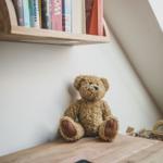 Ein Teddybär sitzt auf einem Holztisch unter einem Bücherregal.