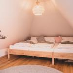Schlafzimmer mit Doppelbett, Holzboden und Wandleuchte unter schrägen Dachdecken.