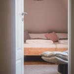 Schlafzimmer mit Bett, Decke und Sitzgelegenheit. Hängelampe und Holzboden.
