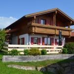 Holzhaus mit Balkon, roten Fensterläden und Gartenzaun.