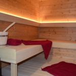 Sauna mit Holzwand, Liegeflächen und roten Handtüchern sowie einem Holzeimer.