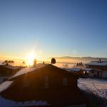 Schneebedeckte Häuser mit Sonnenaufgang über den Bergen.