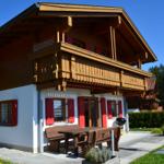 Holzhaus mit Balkon, roten Fensterläden und Gartenmöbeln. Grill und Sonnenschirm vorhanden.