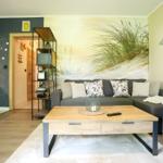 Wohnzimmer mit Sofa, Couchtisch und Küchenbereich. Wandbild mit Strandmotiv.