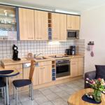Küche mit Essplatz und Wohnbereich mit Sofa und Blumen.