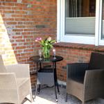 Terrasse mit Tisch und zwei Stühlen, Blumen und Gläser auf dem Tisch.
