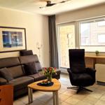 Wohnzimmer mit Sofa, Sessel, Tisch und Fenster. Wandbild und Blumen sind sichtbar.