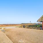 House with thatched roof and stone wall. View of fields and sky.