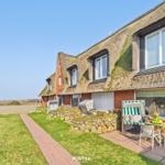 House with thatched roof, terrace with seating and view of grassy area.