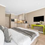Bedroom with bed, kitchenette, and TV. Wall art with sun.