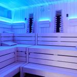 Sauna mit Holzbanken und blauer Beleuchtung an den Wänden.