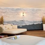 Zimmer mit großem Wandbild eines Meeres und Leuchtturms, Sofa und Holzboden.