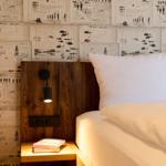 Schlafzimmer mit Holzkopfteil, Wand mit Briefmotiven und Nachttisch mit Buch.