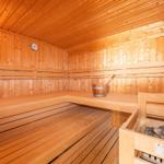 Holzsauna mit Sitzbänken, Eimer und Steinen.