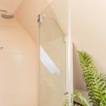 Dusche mit Glaswand und Duschkopf. Pflanze im Vordergrund.