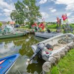 Mehrere Boote liegen an einem Hafen mit grünem Ufer und roten Flaggen.