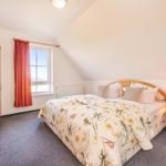 Schlafzimmer mit Bett, Nachttisch, Kleiderschrank und Fenster mit Vorhang.