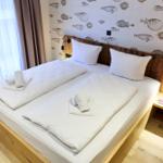 Doppelbett mit weißen Laken und Fischmotiv-Wandtapete.