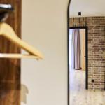 Spiegel zeigt Flur mit Backsteinwand und Holzboden. Kleiderhaken im Vordergrund.