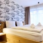 Schlafzimmer mit Holzbett, Segelyacht-Wandtapete und großem Fenster mit Vorhängen.
