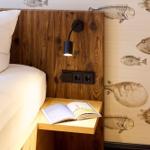 Bettkopfteil aus Holz, Wand mit Fischmotiven, Nachttisch mit Buch und Lampe.