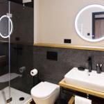 Badezimmer mit Dusche, Waschbecken und Toilette. Runde Spiegel mit Beleuchtung.