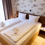 Doppelbett mit weißen Laken, Fischmotiv-Wand und Holzrahmen.
