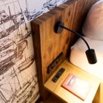 Schlafzimmer mit Holzgestell, Schiffsmotivwand und Nachttisch mit Fernbedienung und Buch.