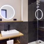 Badezimmer mit Dusche, Waschbecken und beleuchtetem Spiegel.