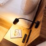 Schlafzimmer mit Holzbett, Nachttisch, Fernbedienung und Glas. Wandlampe beleuchtet die Ecke.